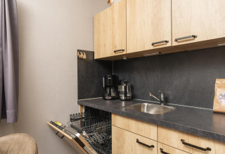 Cocina en Heather Lodge en Veluwepark de Bosgraaf, Países Bajos, con lavavajillas, fregadero y cafeteras.