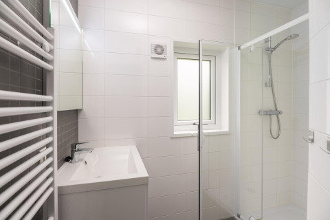Strakke badkamer met glazen douche, wastafel, witte tegels en een raam bij Heather Lodge, Veluwepark.