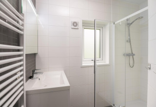 Baño moderno con ducha de vidrio, lavabo cuadrado, azulejos blancos y ventana en Heather Lodge, Veluwe.
