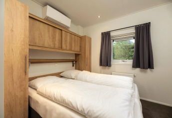 Schlafzimmer in der Heather Lodge im Veluwepark de Bosgraaf, Niederlande, mit Doppelbett und Fenster.