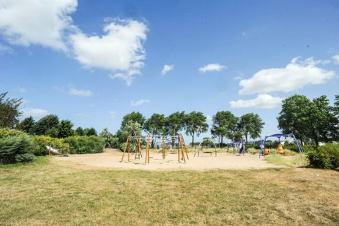 Zicht op een speelplein met schommels en klimrekken, omgeven door groen op Kompas Camping Nieuwpoort.