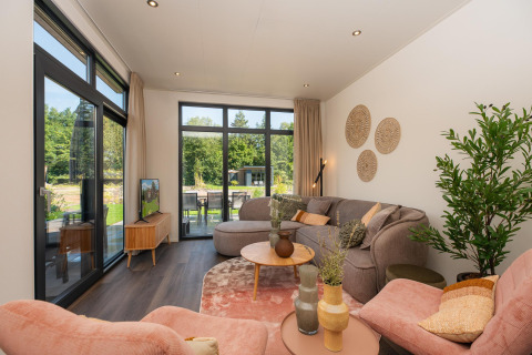 Salón moderno de lodge con grandes ventanales, sofás cómodos, plantas de interior y vistas al jardín.