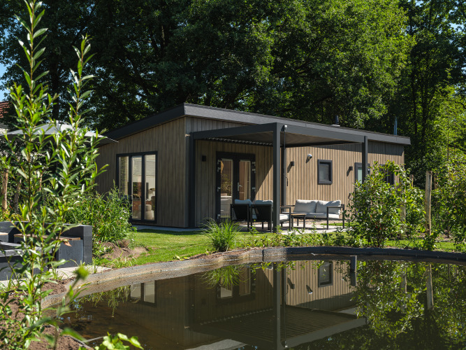 Loevestein Deluxe Lodge mit Whirlpool, moderne Design, Terrasse und Teich inmitten grüner Natur.