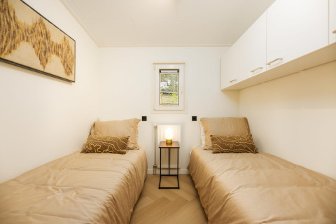 Slaapkamer met twee eenpersoonsbedden, beige lakens en moderne kunst in Loevestein Deluxe, Veluwepark de Bosgraaf.