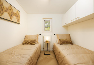 Slaapkamer met twee eenpersoonsbedden, beige beddengoed en moderne kunst in Loevestein Deluxe, Veluwepark de Bosgraaf.