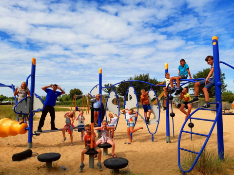 Kinderen spelen en klimmen op kleurrijke speeltoestellen in het zand bij Kompas Camping Nieuwpoort.