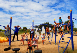 Kinderen spelen en klimmen op kleurrijke speeltoestellen in het zand bij Kompas Camping Nieuwpoort.