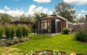 Moderne Lodge mit Terrasse und Sonnenschirm, umgeben von Garten, im Veluwepark de Bosgraaf, Niederlande.