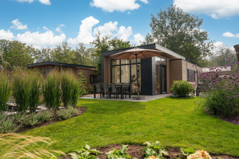 Lodge moderno con arredi da esterno e ombrellone in un giardino verde al Veluwepark de Bosgraaf, Paesi Bassi.