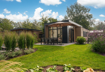 Moderne Lodge mit Terrasse und Sonnenschirm, umgeben von Garten, im Veluwepark de Bosgraaf, Niederlande.