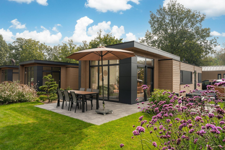 Außenansicht der Lodge Cannenburch mit Whirlpool im Veluwepark de Bosgraaf in den Niederlanden, Blumen ringsum.