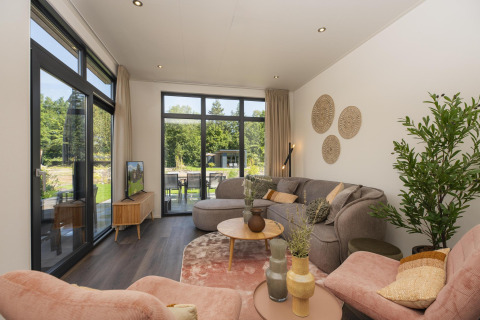 Soggiorno nel lodge Cannenburch, Veluwepark de Bosgraaf, Paesi Bassi, con ampie vetrate e vista giardino.
