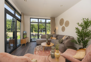 Salón en la cabaña Cannenburch, Veluwepark de Bosgraaf, Países Bajos, con vistas al jardín y muebles cómodos.