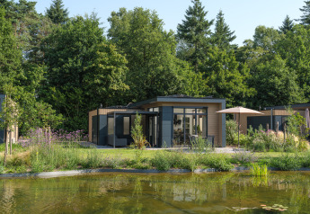 Moderno lodge junto a un estanque rodeado de árboles y plantas en Essenburgh Comfort, Veluwepark de Bosgraaf.