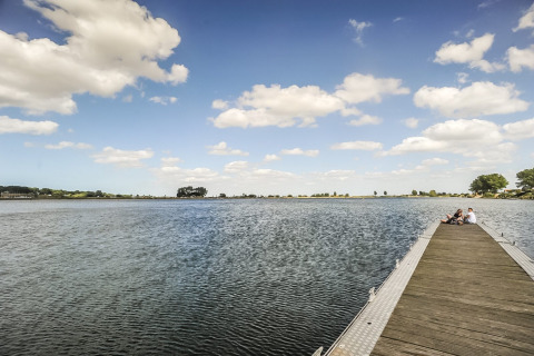 Uitgestrekte houten steiger bij Kompas Camping Nieuwpoort met mensen zittend aan het water in België.