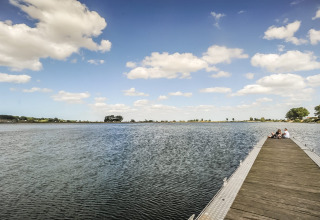 Uitgestrekte houten steiger bij Kompas Camping Nieuwpoort met mensen zittend aan het water in België.