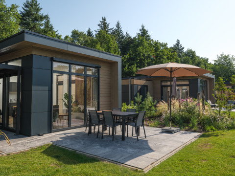 Moderne lodge met terras en parasol in Veluwepark de Bosgraaf, omgeven door natuur en planten.