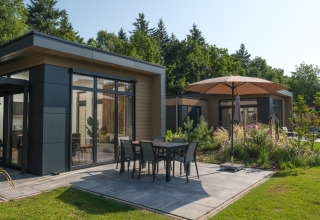 Lodge moderno con patio y sombrilla en Veluwepark de Bosgraaf, rodeado de vegetación y naturaleza.