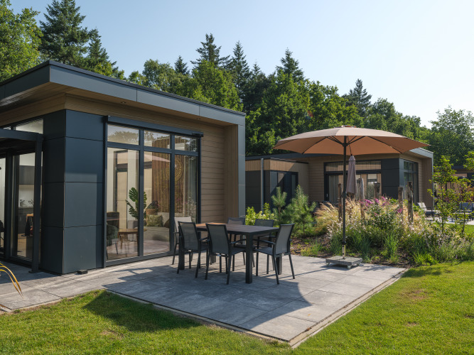Lodge moderno con patio y sombrilla en Veluwepark de Bosgraaf, rodeado de vegetación y naturaleza.