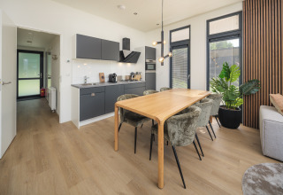 Interior moderno de lodge con cocina abierta, mesa de comedor y grandes ventanas en Veluwepark de Bosgraaf, Países Bajos.