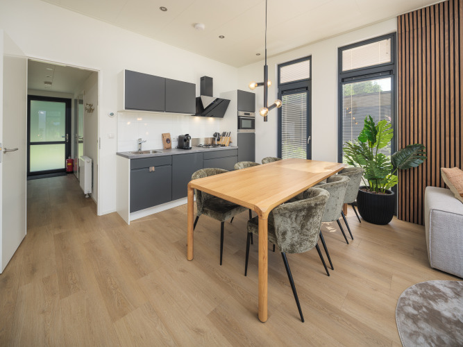 Interior moderno de lodge con cocina abierta, mesa de comedor y grandes ventanas en Veluwepark de Bosgraaf, Países Bajos.