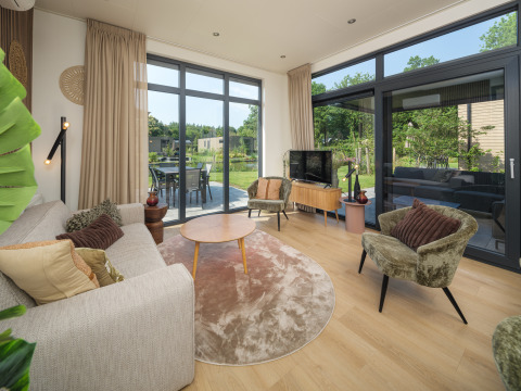 Modernes Wohnzimmer der Essenburgh Comfort Lodge im Veluwepark de Bosgraaf, Niederlande, mit Gartenblick.