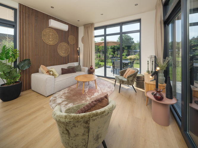Sala moderna en una cabaña en Veluwepark de Bosgraaf, Países Bajos, con grandes ventanales y vista al jardín.