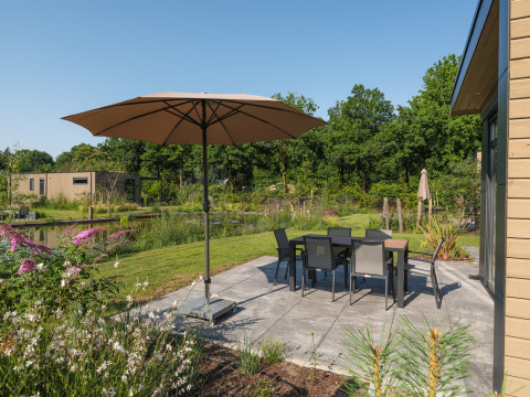 Zonnig terras met parasol en tuinset bij Essenburgh Comfort lodge in Veluwepark de Bosgraaf, Nederland.