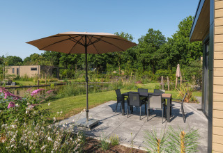 Terraza soleada con sombrilla grande y muebles de jardín en Essenburgh Comfort en Veluwepark de Bosgraaf, Países Bajos.