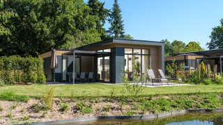 Moderne Essenburgh Comfort Lodge mit Whirlpool, Sonnenliegen und Terrasse am Teich in grüner Umgebung.