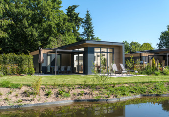 Moderne Essenburgh Comfort Lodge mit Whirlpool, Sonnenliegen und Terrasse am Teich in grüner Umgebung.
