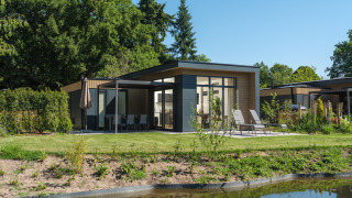 Lodge moderne Essenburgh Comfort avec bain à remous, transats et terrasse, entourée de verdure et d’un étang.
