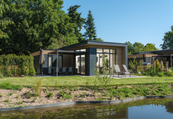 Lodge Essenburgh Comfort moderno con jacuzzi, tumbonas y terraza, rodeado de vegetación y un estanque.