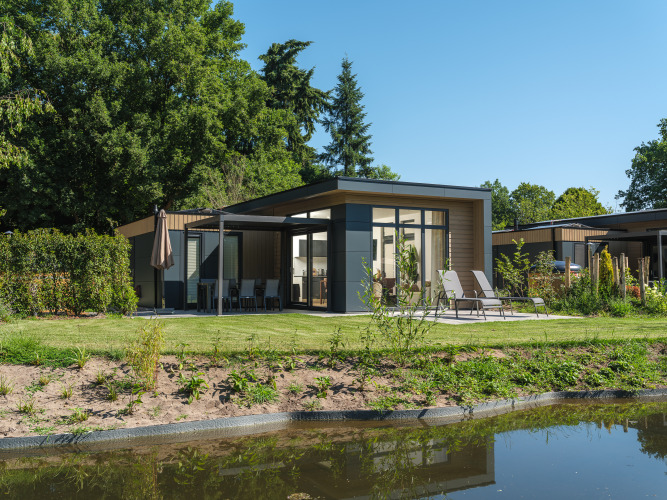 Moderne Essenburgh Comfort lodge met hottub, ligbedden en terras, omgeven door groen en een vijver.