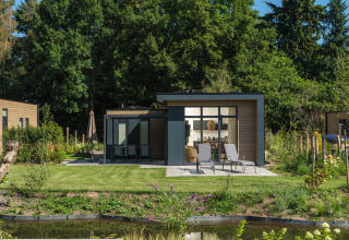 Modern Essenburgh Comfort lodge with patio, loungers, and lush garden at Veluwepark de Bosgraaf, Netherlands.