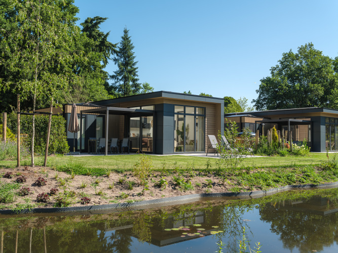 Lodge Essenburgh Comfort moderno con jacuzzi en Veluwepark de Bosgraaf, Países Bajos, junto a un estanque.