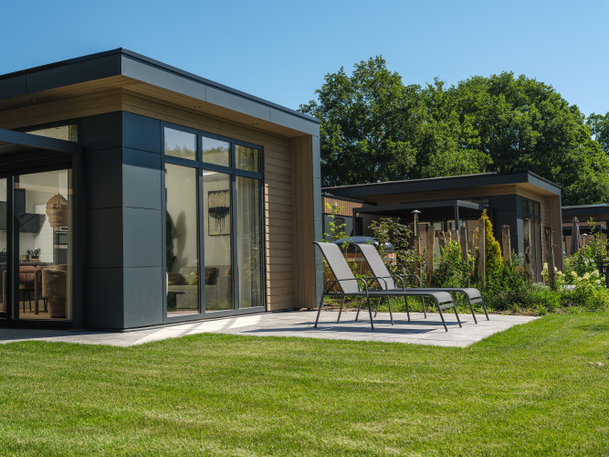 Moderne Lodge mit großen Fenstern, Sonnenliegen und gepflegtem Rasen im Veluwepark de Bosgraaf, Niederlande.