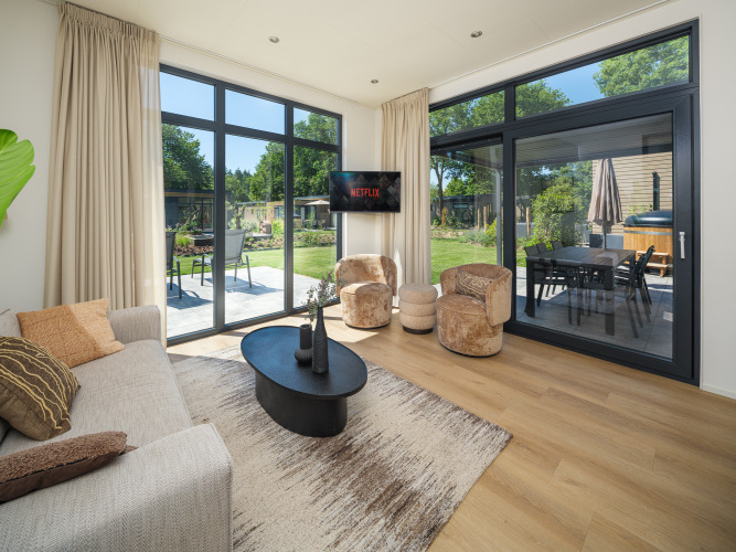 Stijlvolle woonkamer van Essenburgh Comfort lodge met tuinzicht en hottub op Veluwepark de Bosgraaf.
