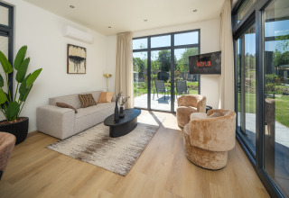 Salón moderno en la lodge Essenburgh Comfort con ventanales, asientos cómodos y vista al jardín en Veluwepark de Bosgraaf.