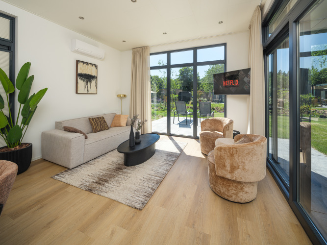 Moderne woonkamer van Essenburgh Comfort lodge met grote ramen, tuinzicht en hot tub in Veluwepark de Bosgraaf.