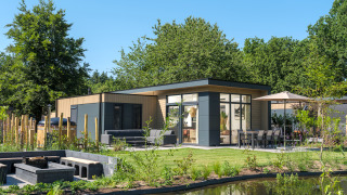 Moderne Essenburgh Deluxe Lodge mit Whirlpool, Terrasse, Gartenmöbeln und Teich, umgeben von Natur.