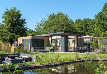 Moderno lodge Essenburgh Deluxe con jacuzzi, área de comedor exterior y estanque en entorno natural.