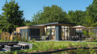 Modern Essenburgh Deluxe lodge with hot tub, outdoor seating, dining area, and pond in a natural setting.