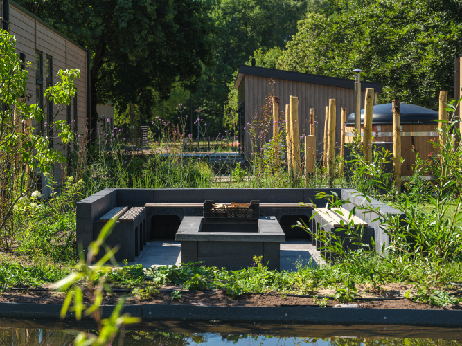 Gemütlicher Außenbereich mit Feuerstelle und viel Grün am Essenburgh Deluxe mit Whirlpool in den Niederlanden.