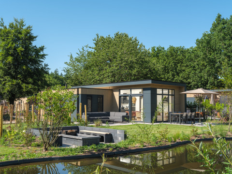 Modern Essenburgh Deluxe lodge with hot tub at Veluwepark de Bosgraaf, surrounded by garden and pond.