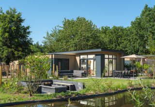 Lodge Essenburgh Deluxe con jacuzzi en Veluwepark de Bosgraaf, rodeada de jardín y estanque natural.
