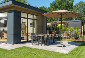 Patio esterno con tavolo da pranzo, sedie e ombrellone presso Essenburgh Deluxe lodge a Veluwepark de Bosgraaf, Paesi Bassi.