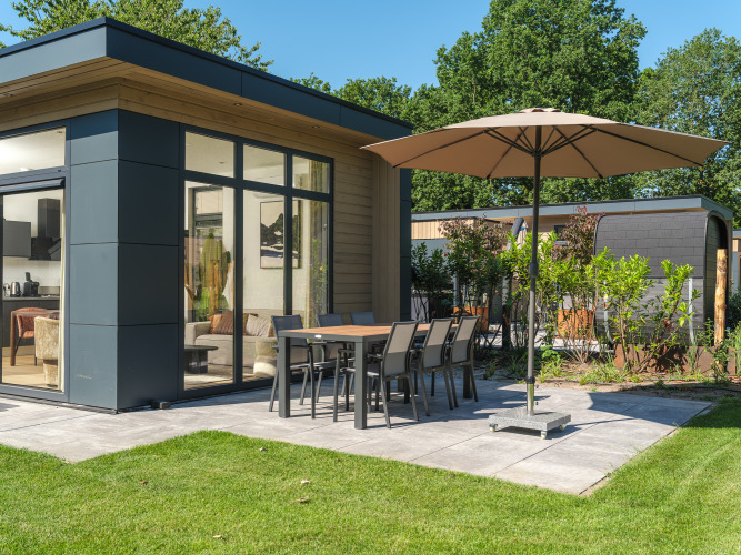 Terrasse mit Esstisch, Stühlen und Sonnenschirm bei der Essenburgh Deluxe Lodge im Veluwepark de Bosgraaf, Niederlande.