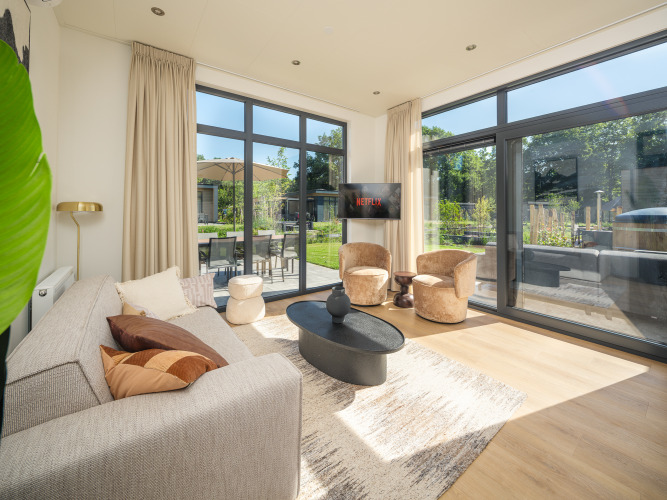 Helles Wohnzimmer in der Essenburgh Deluxe-Lodge mit großen Fenstern und Blick auf den Garten im Veluwepark de Bosgraaf.