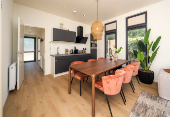 Interior de lodge moderno con cocina, comedor y grandes ventanales en Essenburgh Deluxe, Veluwepark de Bosgraaf, NL.